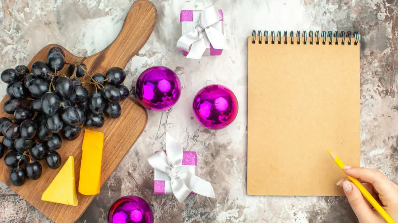vista-superior-del-delicioso-racimo-de-uva-negra-fresca-y-queso-en-la-tabla-de-cortar-de-madera-y-accesorios-de-decoracion-de-regalos-y-escritura-mano-en-el-cuaderno-sobre-fondo-de-color-mezclado